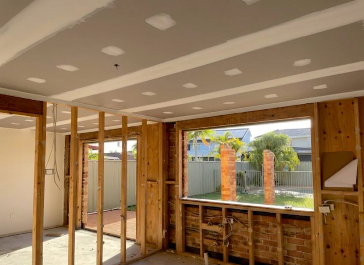 A renovated open plan living area with the new ceiling sheeted and set, and the original wall framing still exposed below it.