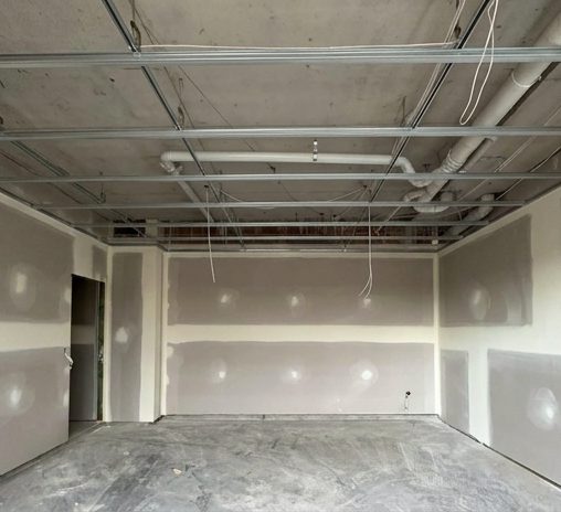 A ceiling dropped below the pipework and ducting in a commercial space, with the walls sheeted and set.